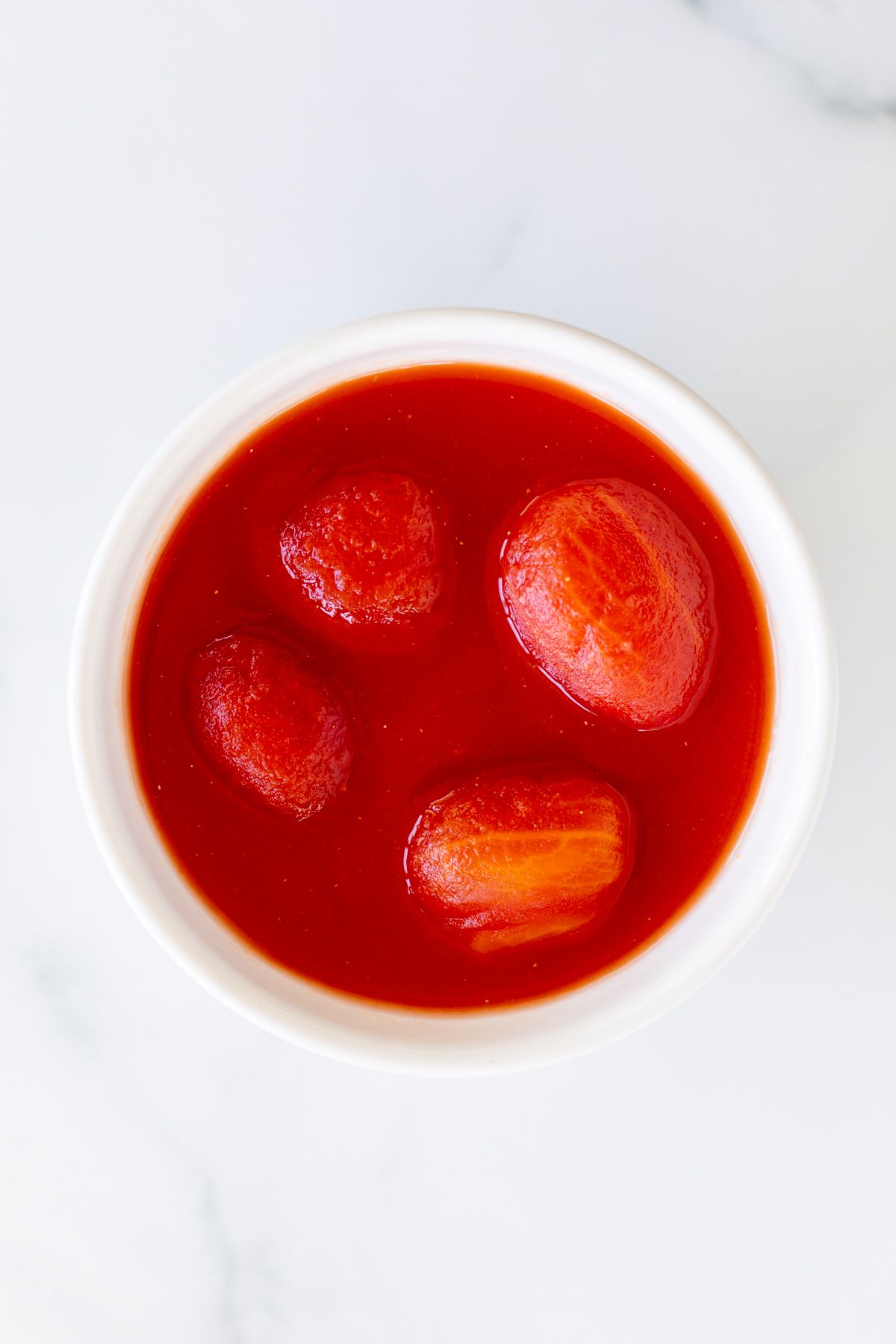 A small white bowl full of stewed tomatoes for a tomato paste substitute.