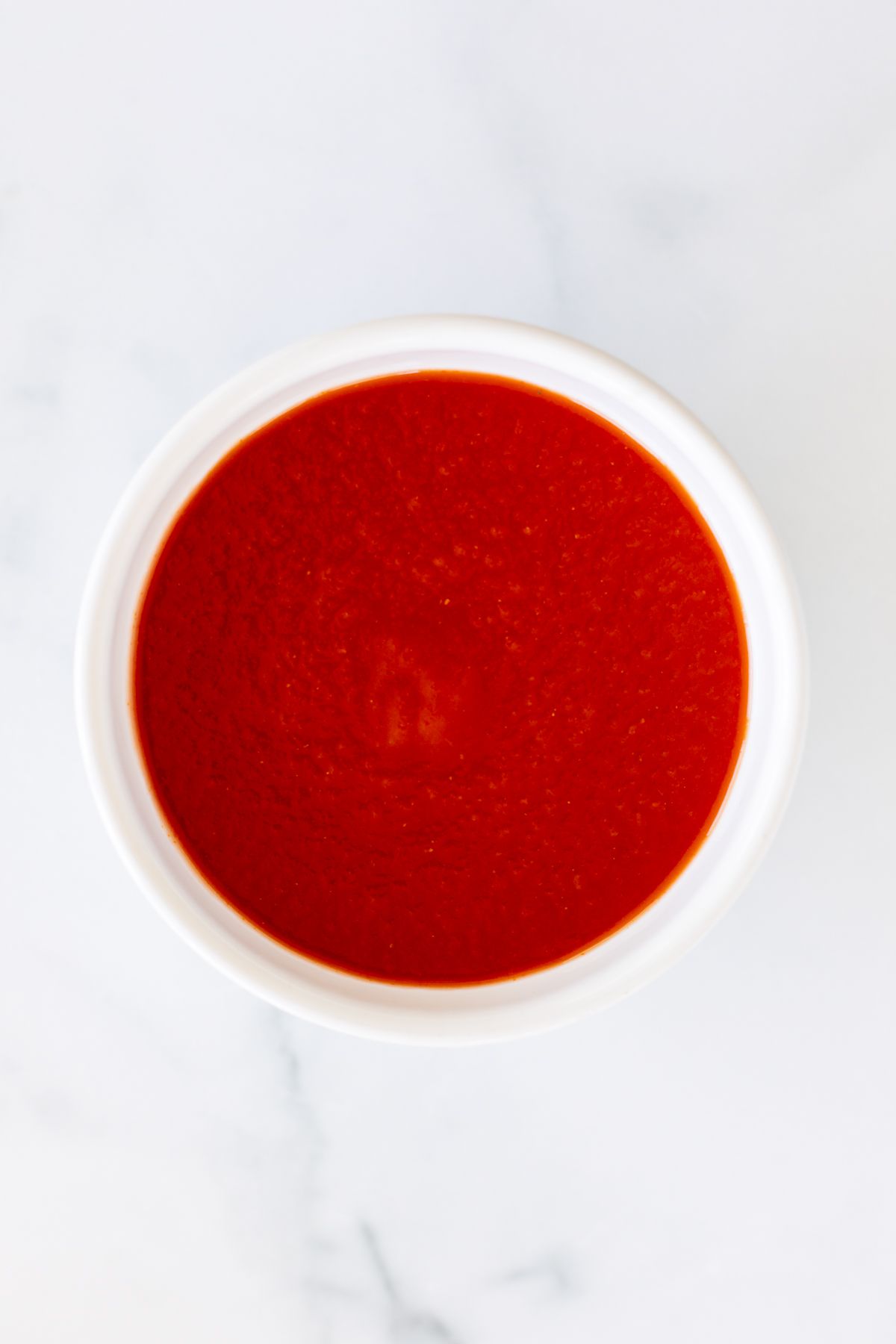 A small white bowl full of tomato sauce for a tomato paste substitute.