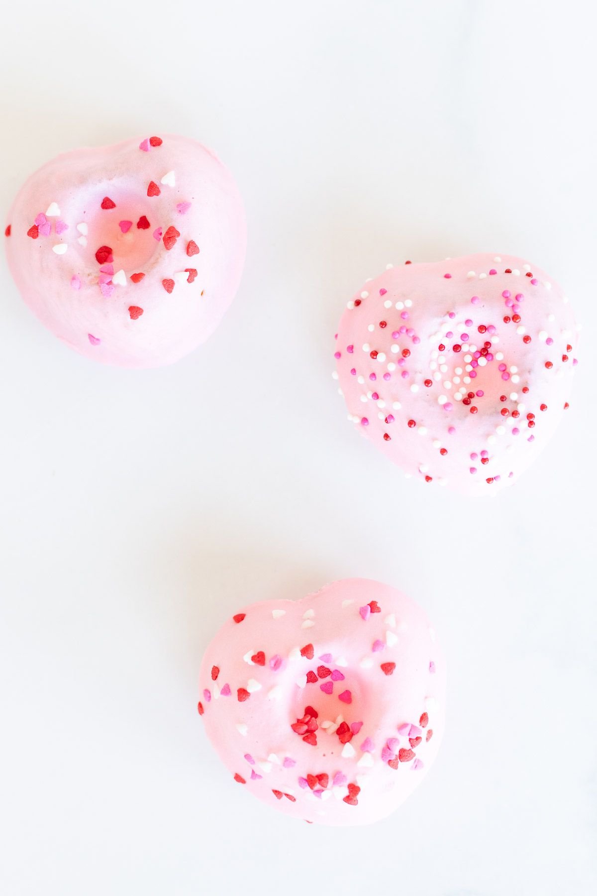 Heart shaped Valentine doughnuts on a white surface, covered in pink icing and sprinkles.