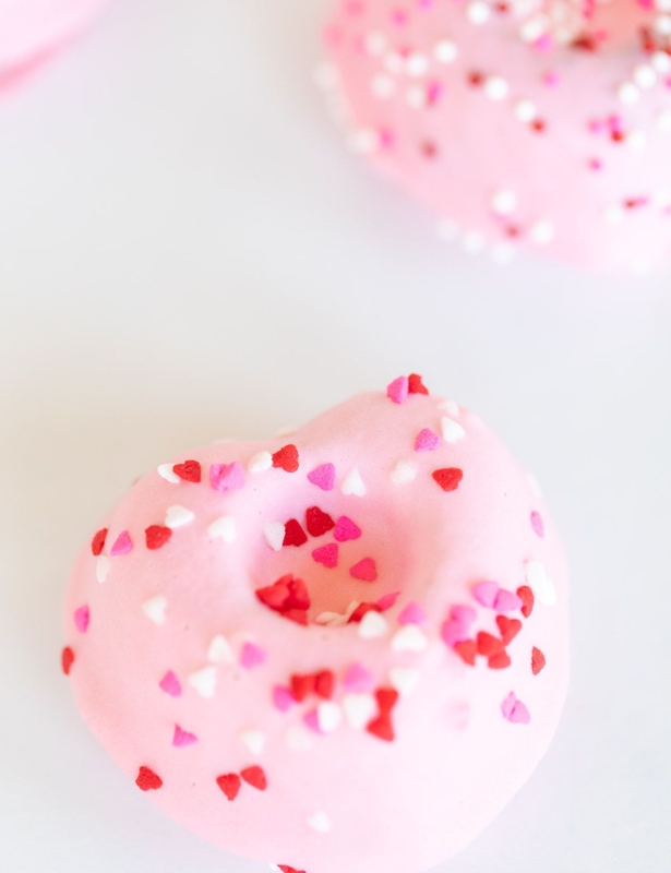 Heart shaped Valentine doughnuts on a white surface, covered in pink icing and sprinkles.
