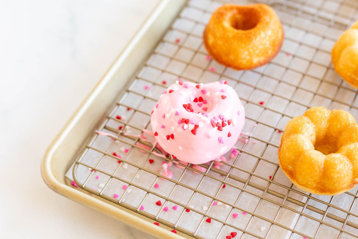 Heart shaped Valentine doughnuts on a baking sheet, covered in pink icing and sprinkles.