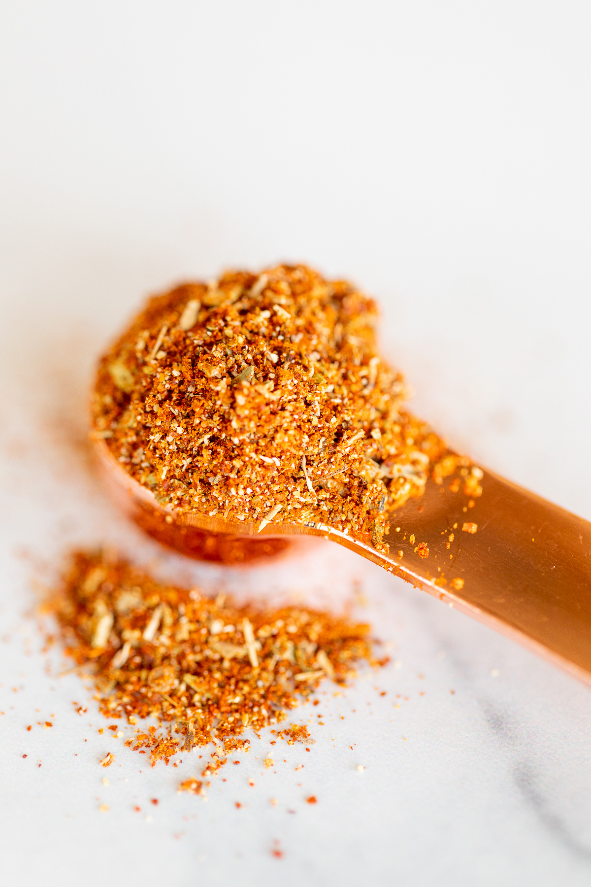 Closeup of chipotle seasoning spilling out of copper measuring spoon