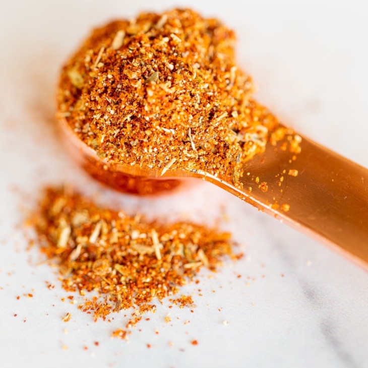 A copper teaspoon full of homemade chipotle seasoning, on a marble countertop.