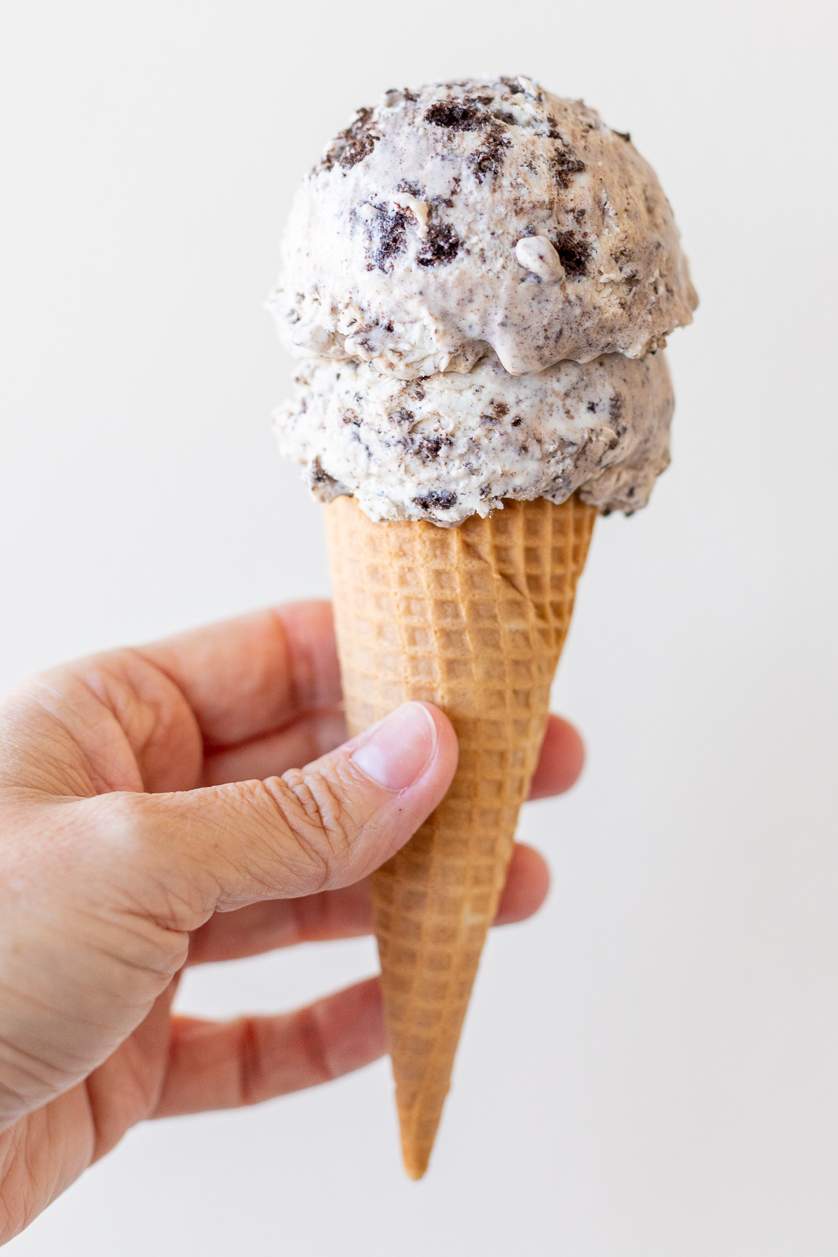 Hand holding cone topped with two scoops of cookies and cream ice cream