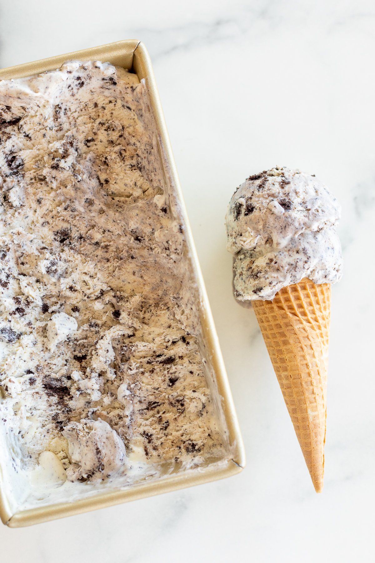 Overhead view of cookies and cream ice cream in loaf pan next to ice cream cone