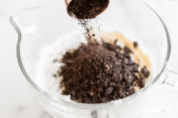 Pouring Oreo crumbs into mixing bowl with no-churn ice cream