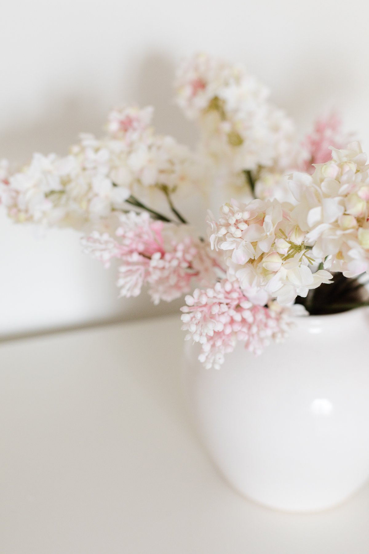 pink and white faux flowers in a white  vase