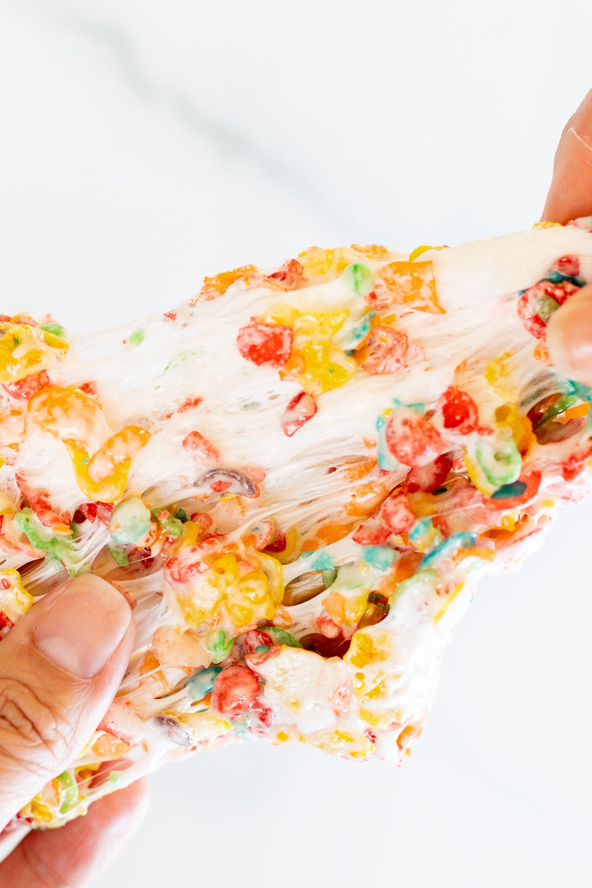 Hands pulling apart a Fruity Pebbles Treat to show chewy marshmallow