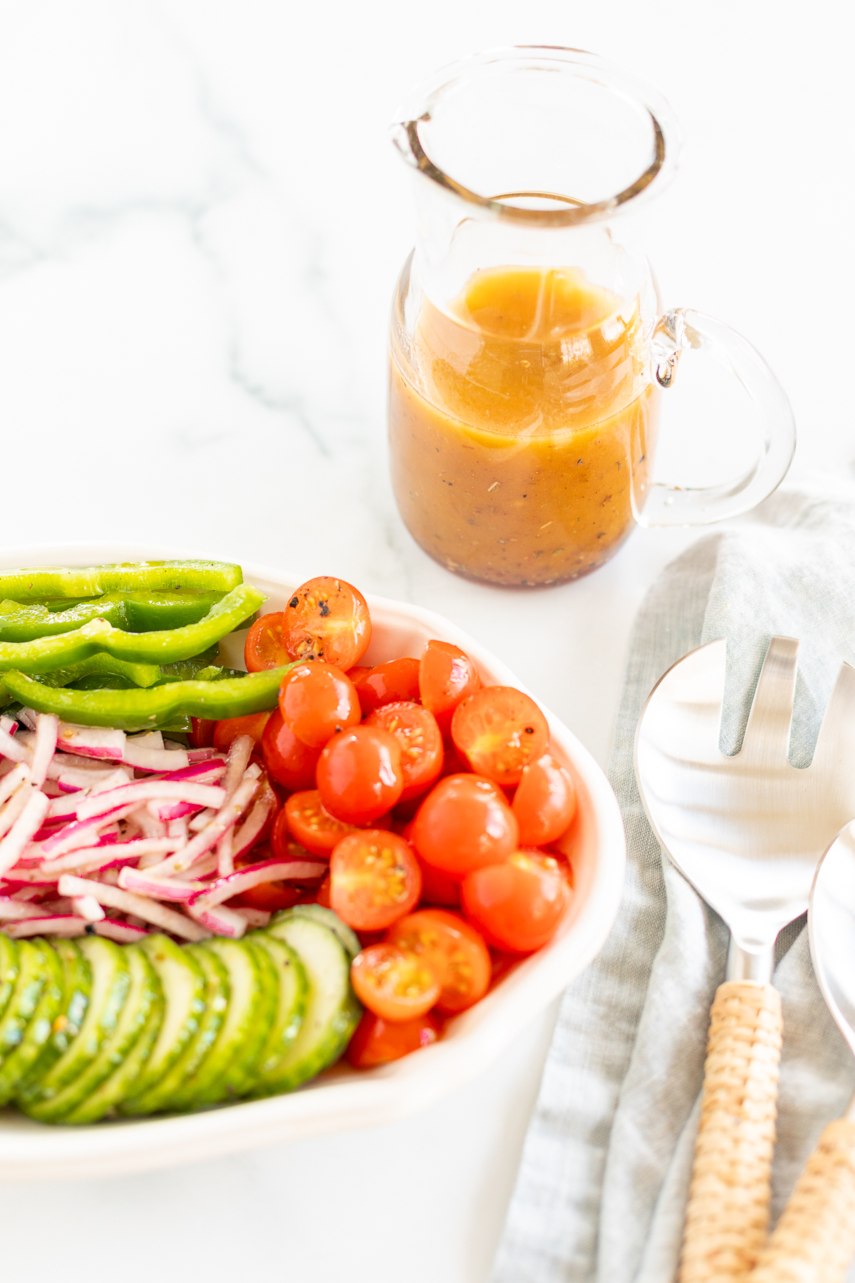 Greek salad vegetables on platter set next to pitcher of red wine vinaigrette and serving utensils