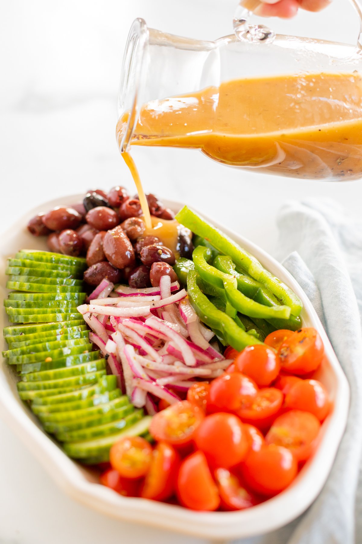 Pouring red wine vinaigrette over platter of vegetables for Greek salad
