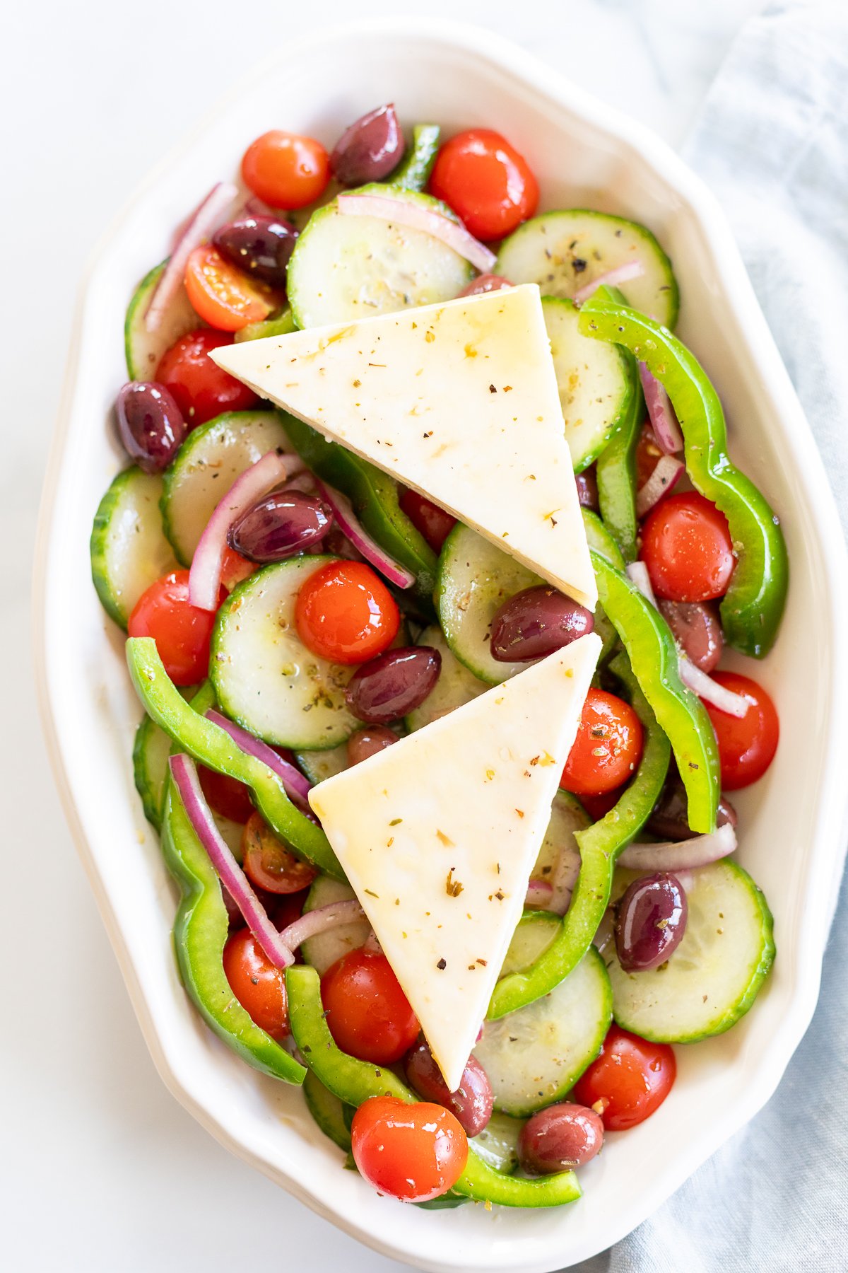 Overhead view of Greek salad on platter with two wedges of feta set over the top