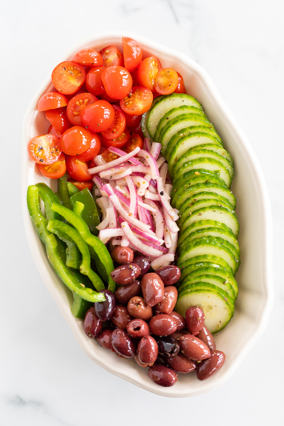Platter with ingredients for Greek salad, including cherry tomatoes, green pepper, red onion, cucumbers, and olives
