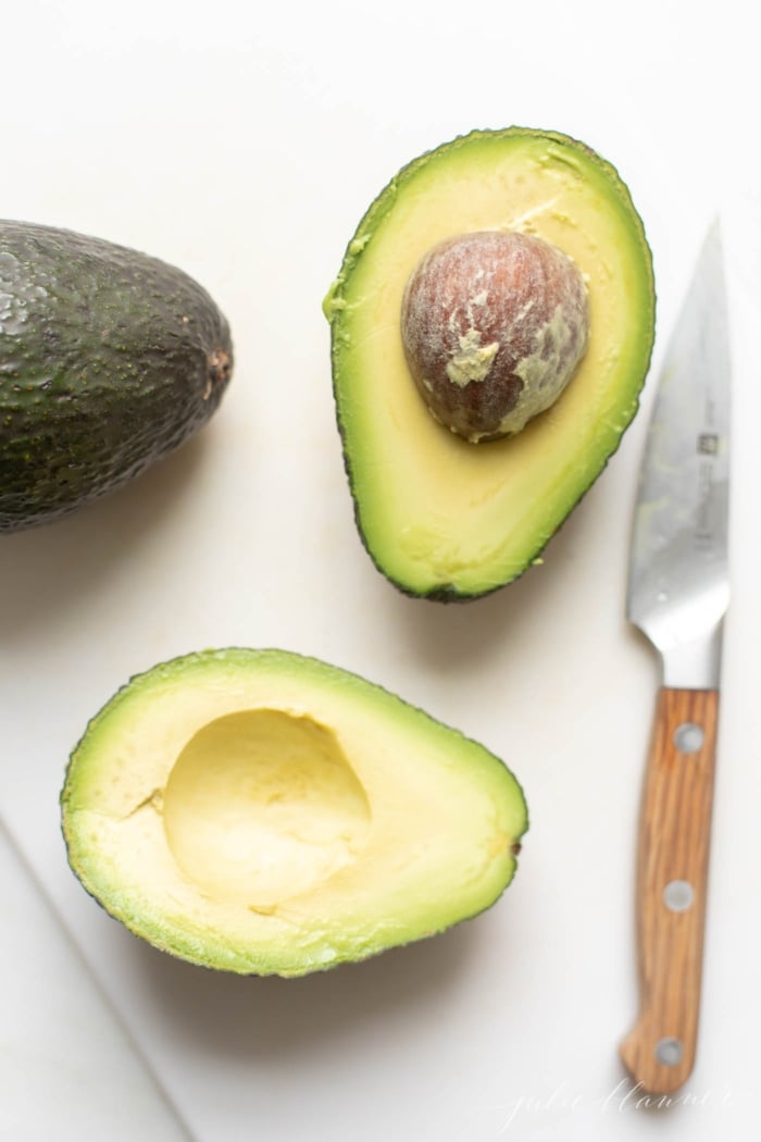 Overhead view of two cut avocado halves with knife
