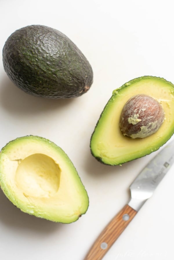 Overhead view of one whole avocado and two cut avocado halves with knife