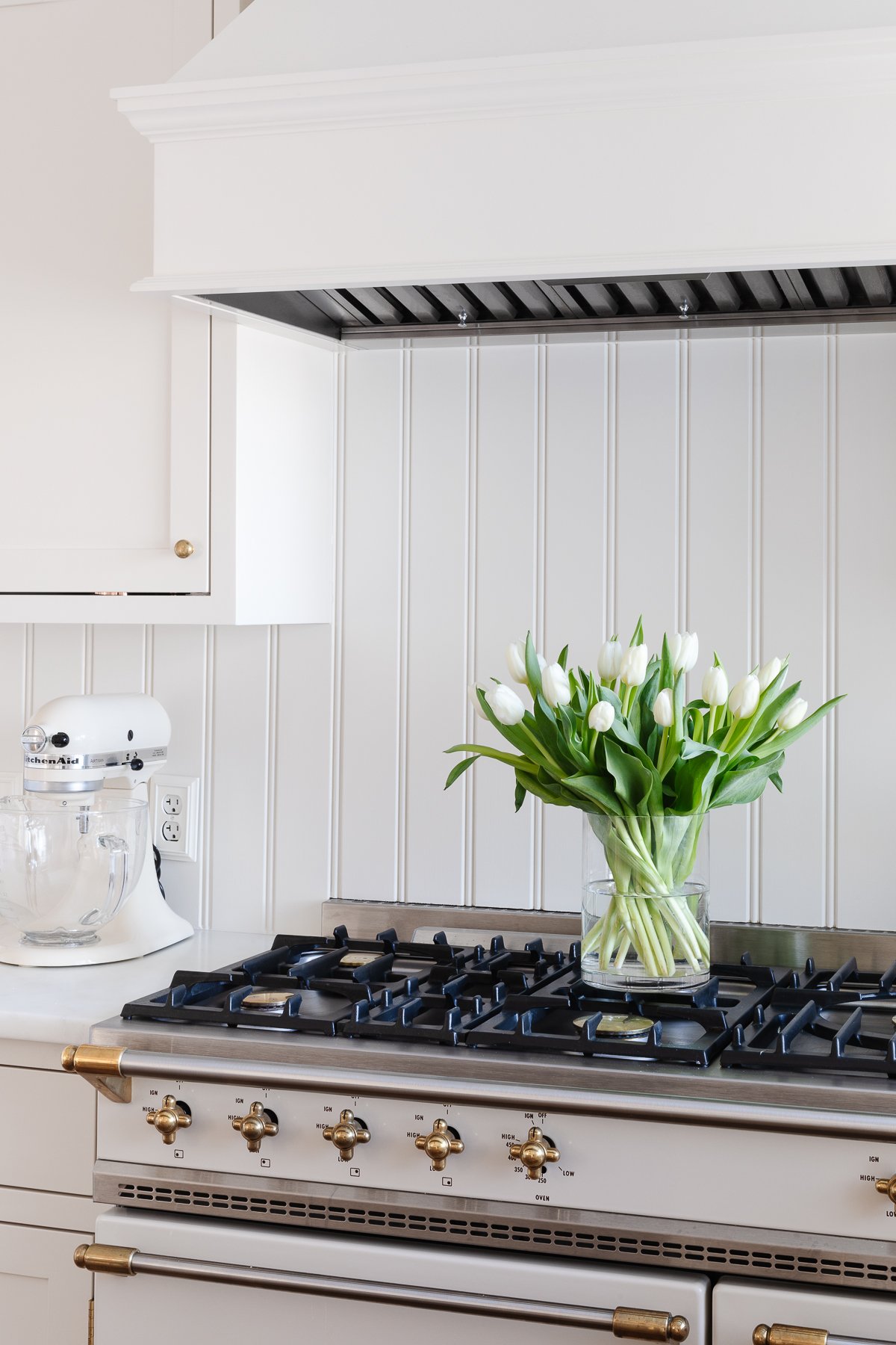 A cream kitchen with a beadboard backsplash and an insert range hood with a wood cover.