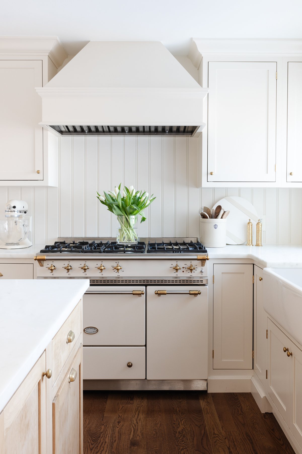 A cream kitchen with a beadboard backsplash and an insert range hood with a wood cover.