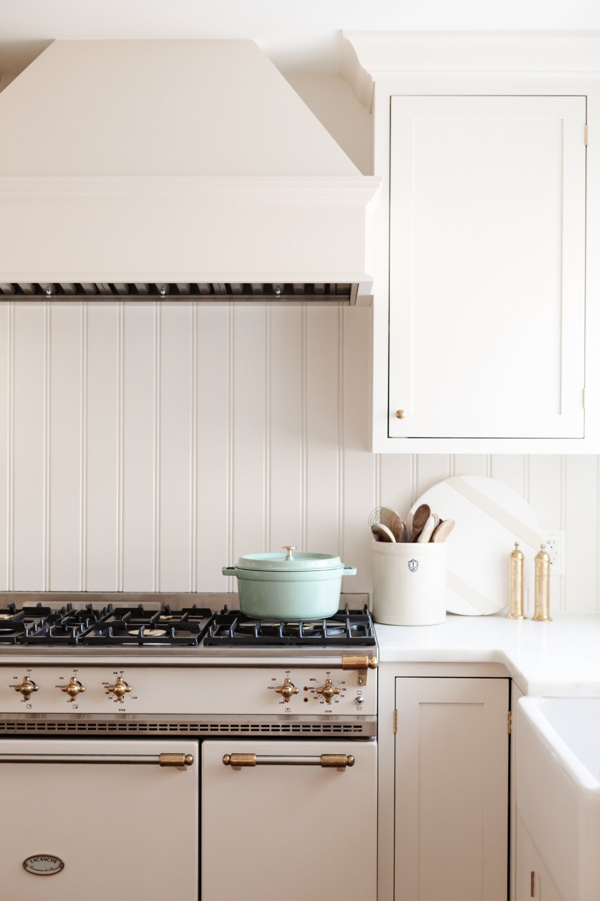 A cream kitchen with a beadboard backsplash and an insert range hood with a wood cover. 