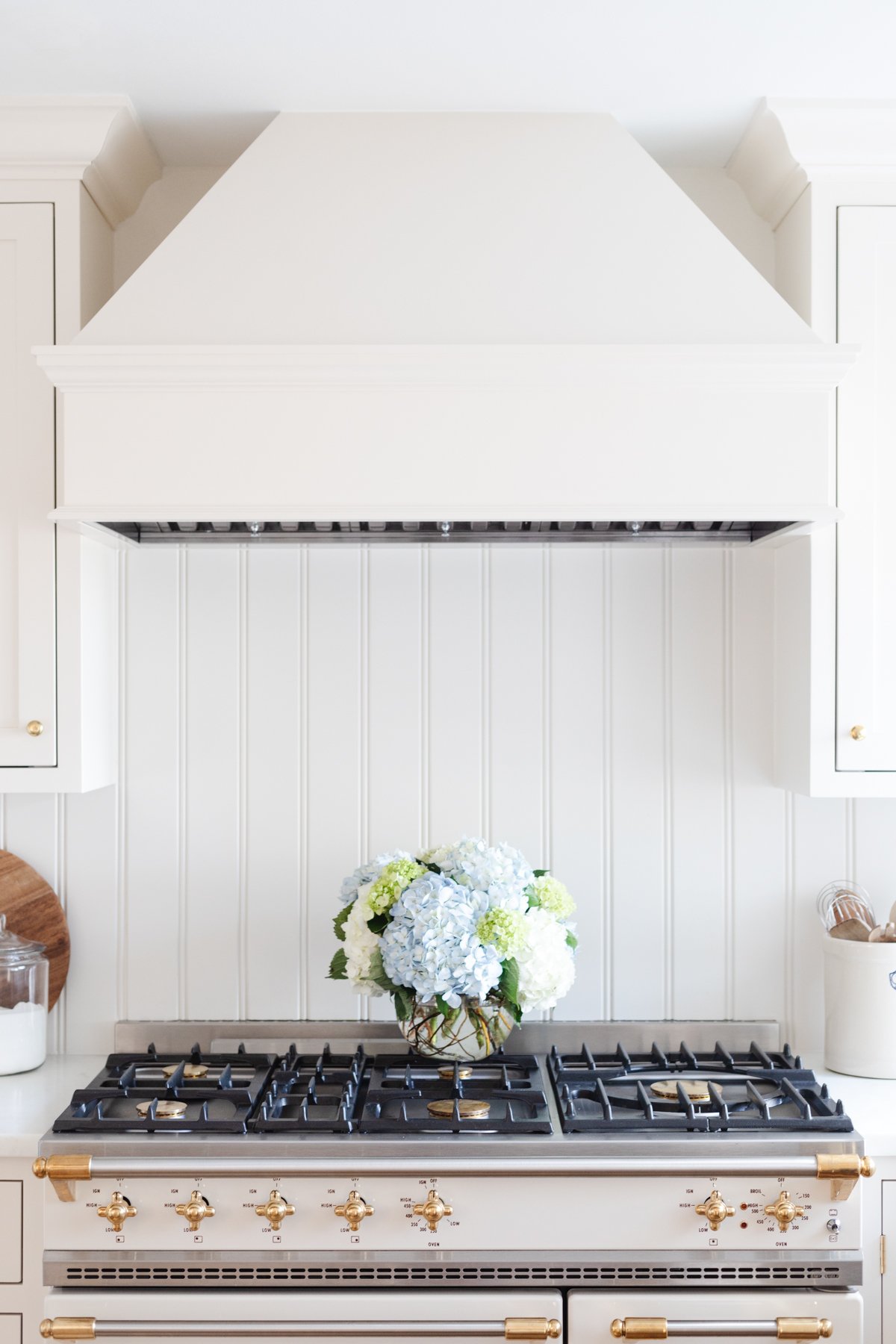 A cream kitchen with a beadboard backsplash and an insert range hood with a wood cover.