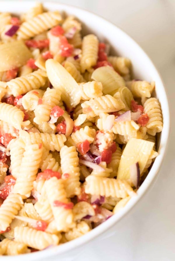 A bowl of Italian pasta salad mixed with diced tomatoes, onions, and a light dressing.