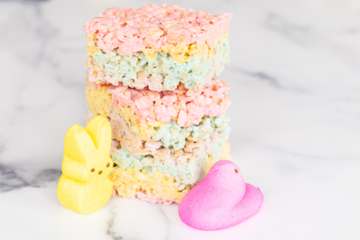 On a marble counter top, there are 3 marshmallow Peep treats stacked on top of one another and a yellow Peep bunny and a pink Peep duck.