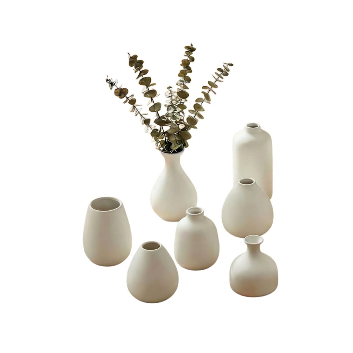 Seven matte white ceramic flower vases of varying shapes are arranged together; one vase holds dried eucalyptus stems. All are set against a white background.