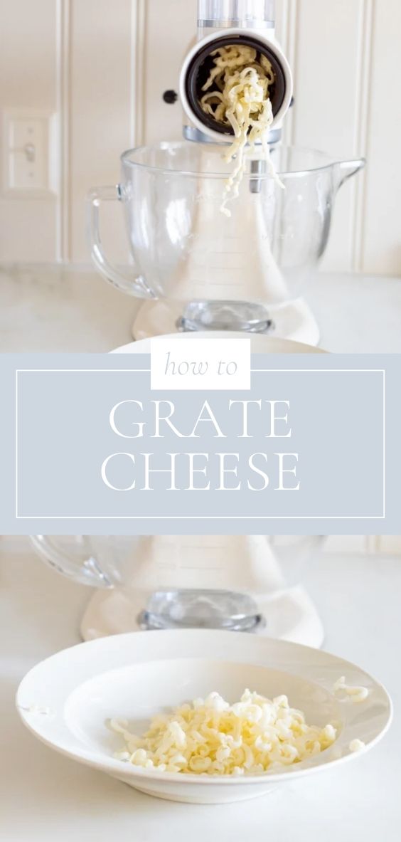 On a marble counter top there is a white mixer with a clear bowl and a grating attachment that is grating a white cheese.