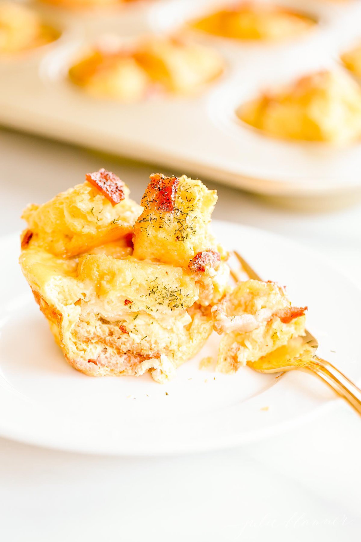 egg strata on a fork with muffin tin in background