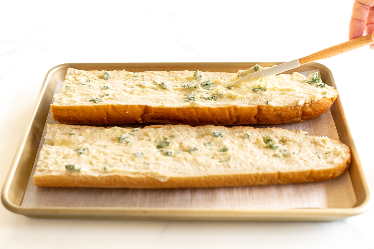 Spreading garlic butter onto two halves of French bread for garlic cheese bread