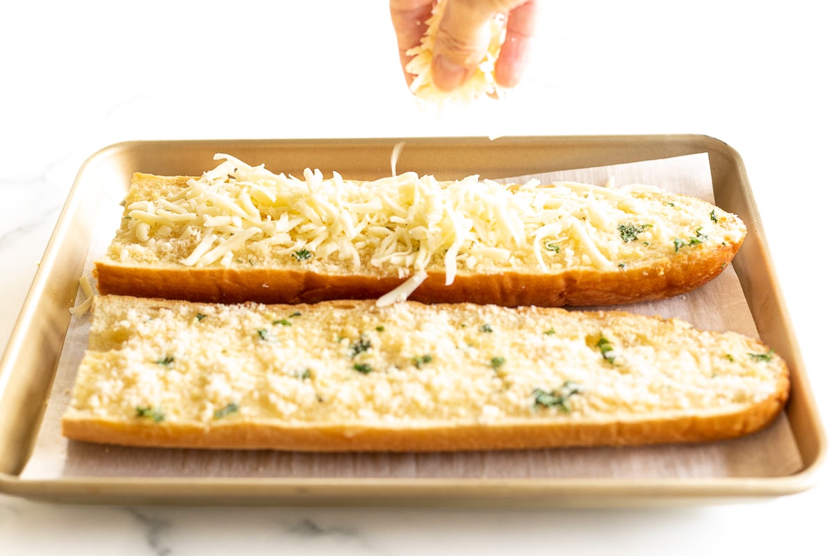 Hand sprinkling shredded mozzarella onto garlic bread