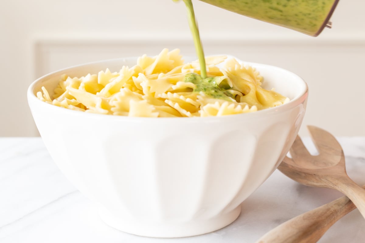 pouring cilantro lime dressing onto pasta in a white bowl