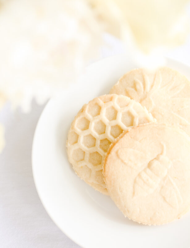 lemon shortbread cookies stamped with flowers, bees and beehives on a white plate