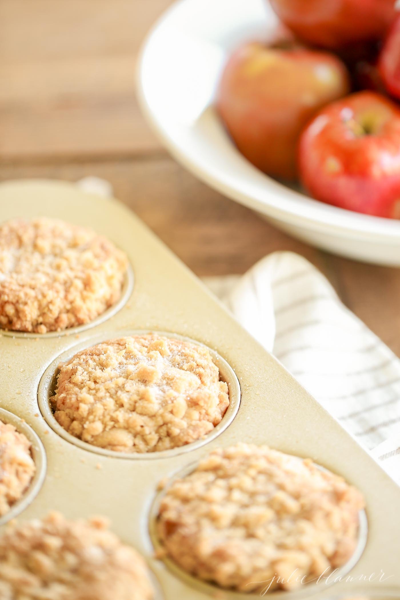 apple cobbler muffins in a gold muffin pan, apples in the background.