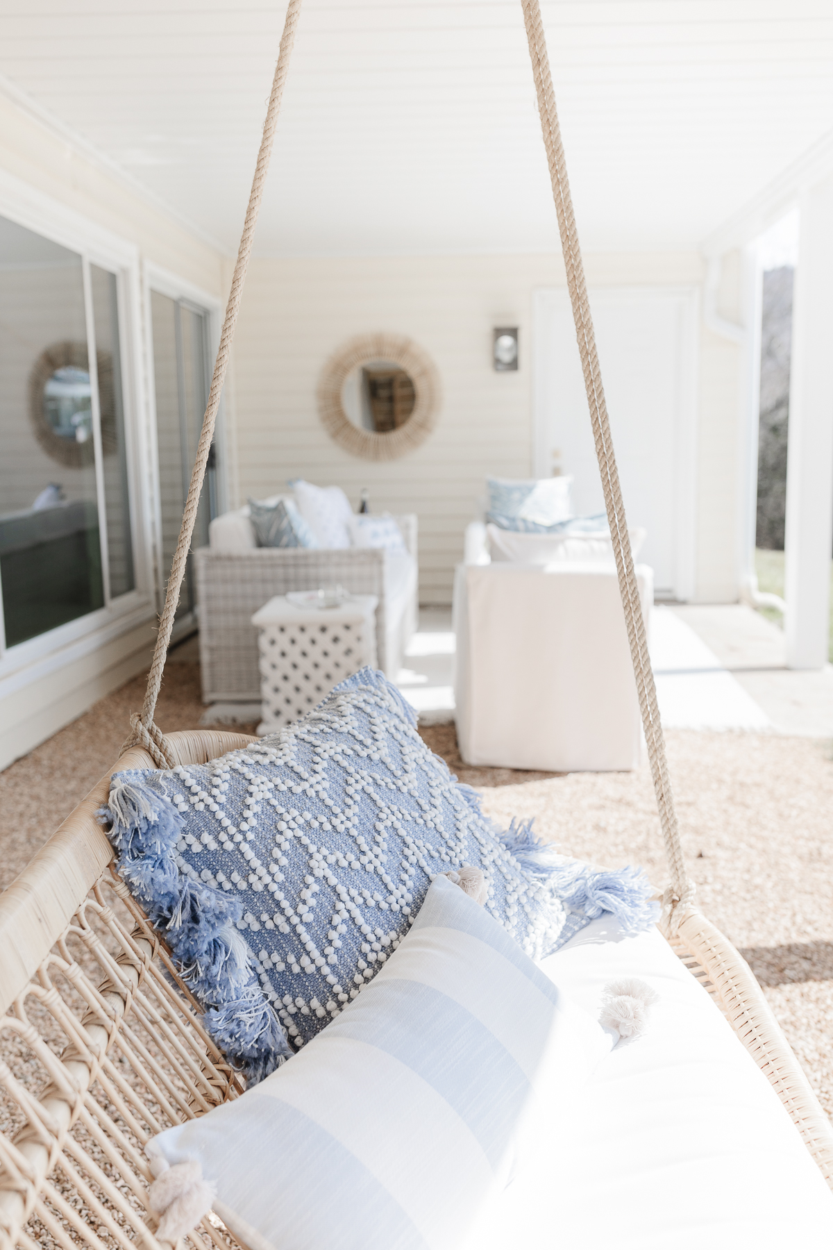 An outdoor patio area with a hanging chair and outdoor pillows in blue and white. 