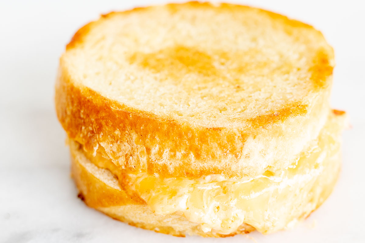 A pimento grilled cheese sandwich on round bread, on a marble countertop.