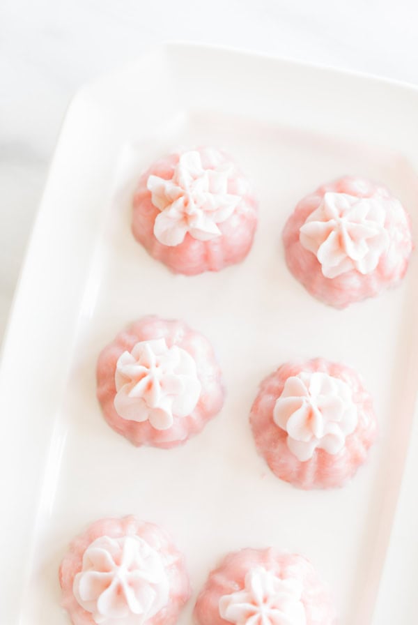 A white rectangular dish holds six pink bundt cakes, each topped with white frosting dollops – perfect for delightful bridal shower recipes.