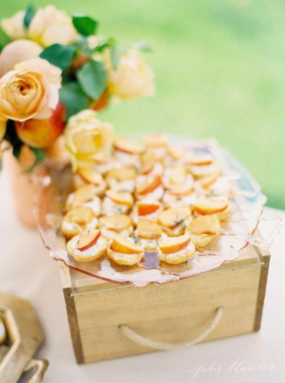 peach crostini on a glass plate with a wooden box.