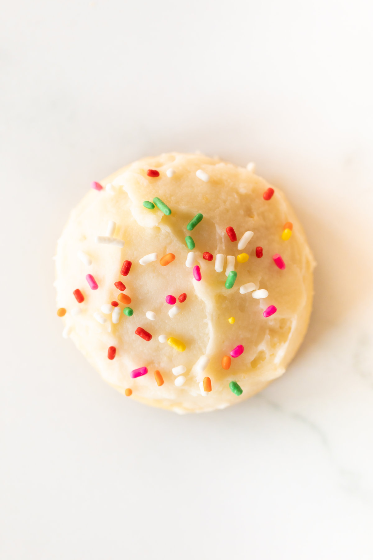 A melt in your mouth sugar cookie frosted with sprinkles on a marble surface.
