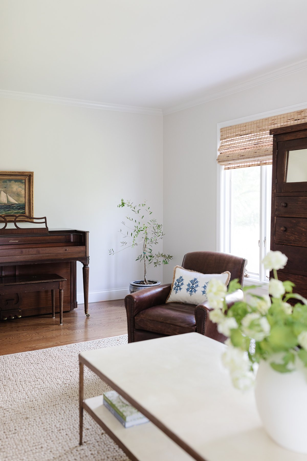 A family room with an antique piano and armoire, leather chairs and bamboo blinds.