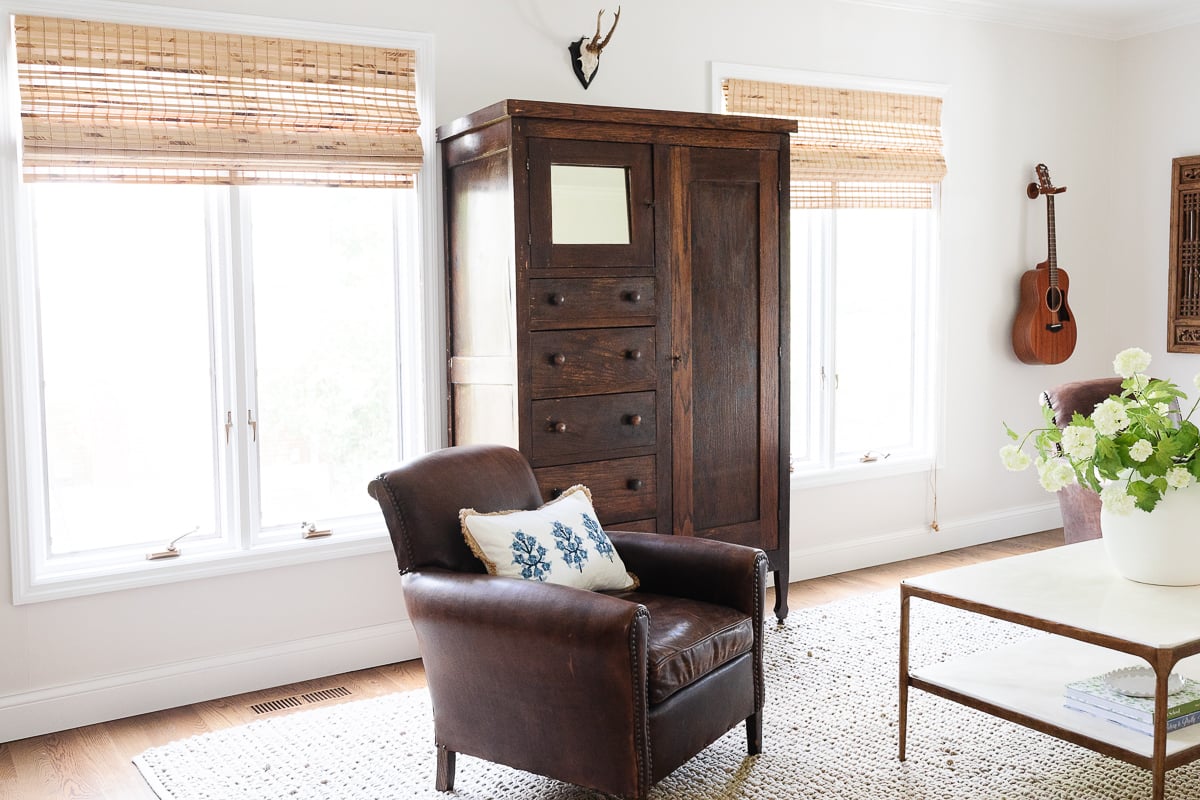 A family room with an antique armoire and bamboo blinds. 