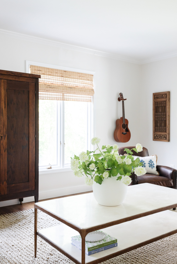 A family room with an antique armoire and bamboo blinds.