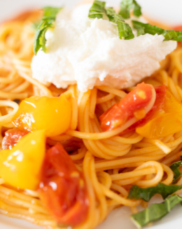 Closeup of spaghetti topped with blistered tomatoes, ricotta, and basil