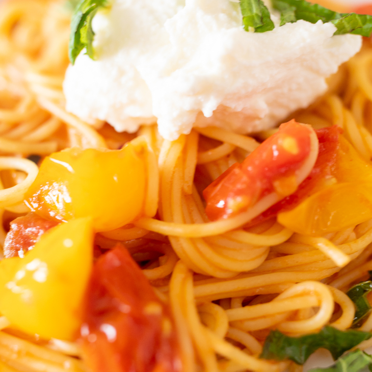 Closeup of spaghetti topped with blistered tomatoes, ricotta, and basil