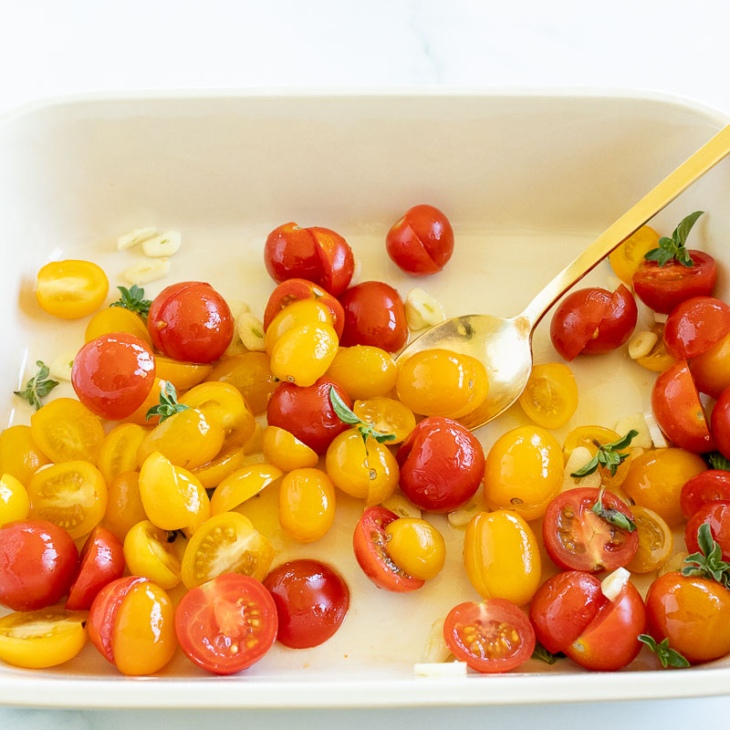 Tomates cherry a la mitad en una fuente para hornear con aceite de oliva y albahaca