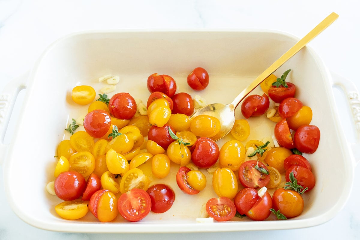 Tomates cherry a la mitad en una fuente para hornear con aceite de oliva y albahaca