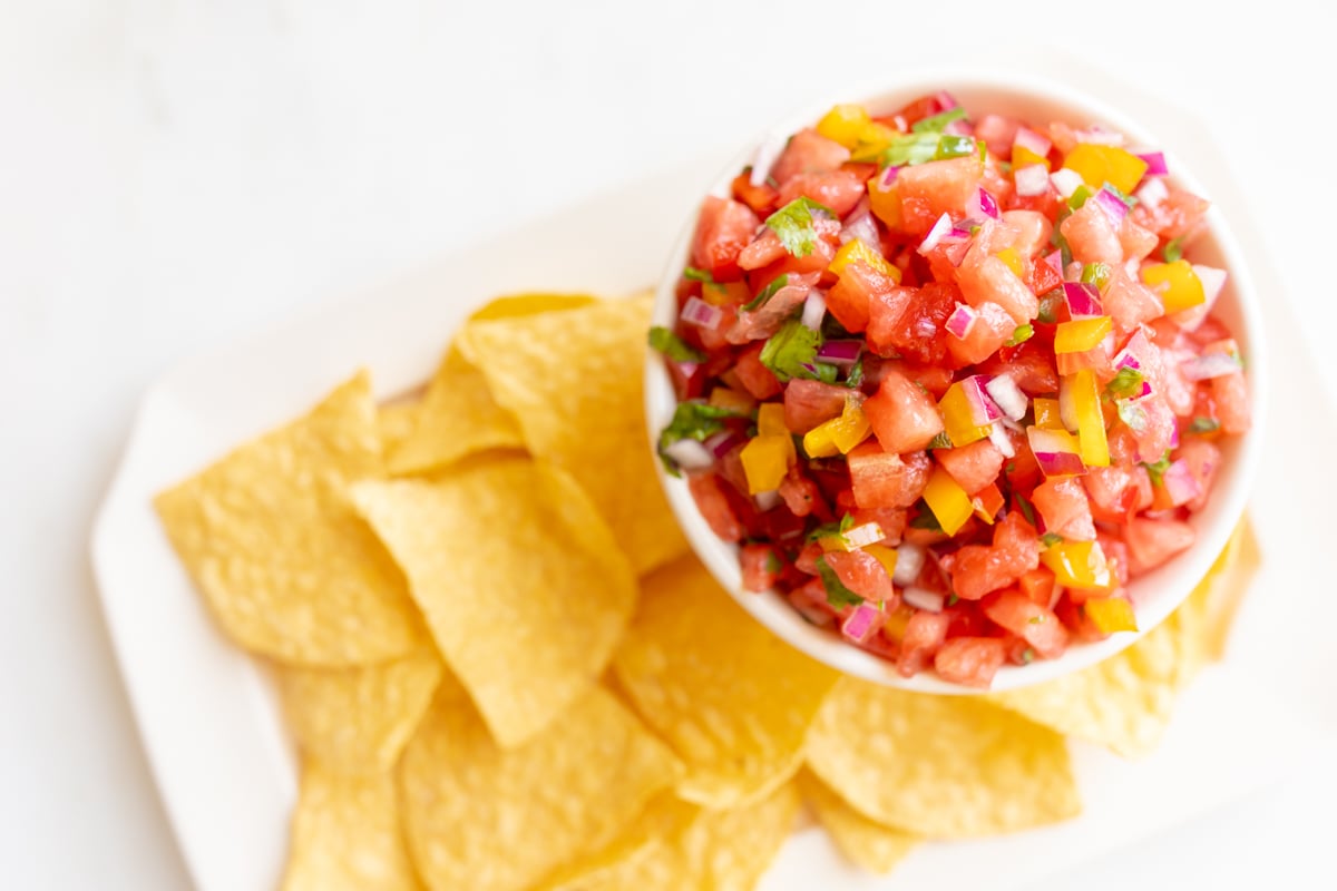 A bowl of watermelon salsa on a plate of tortilla chips.