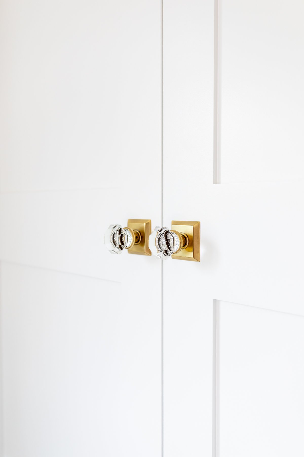 A pair of white shaker closet doors with brass door knobs.