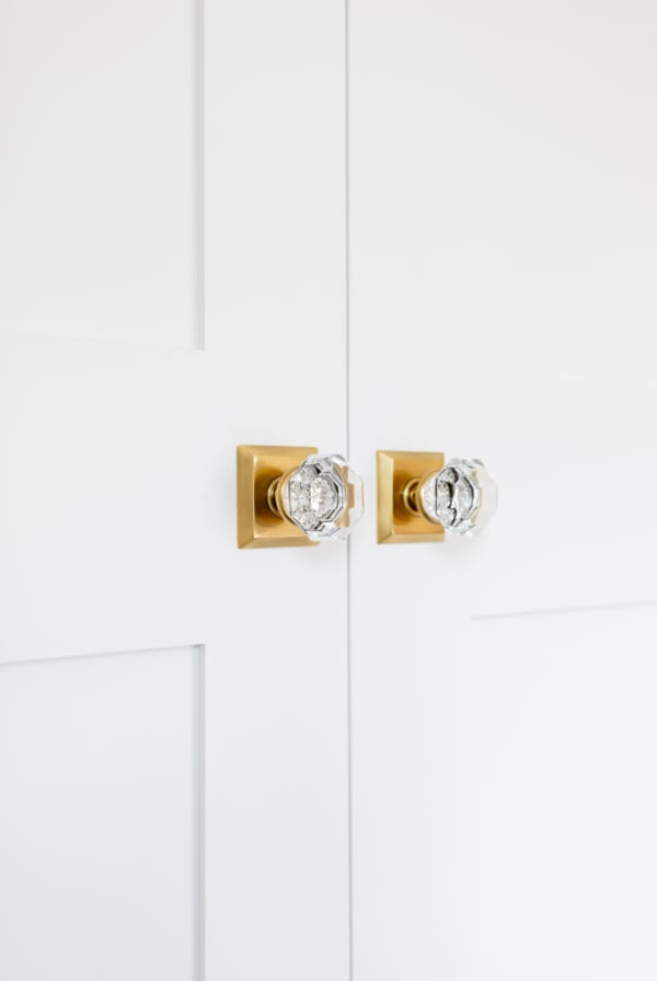 A pair of white shaker closet doors with brass door knobs.