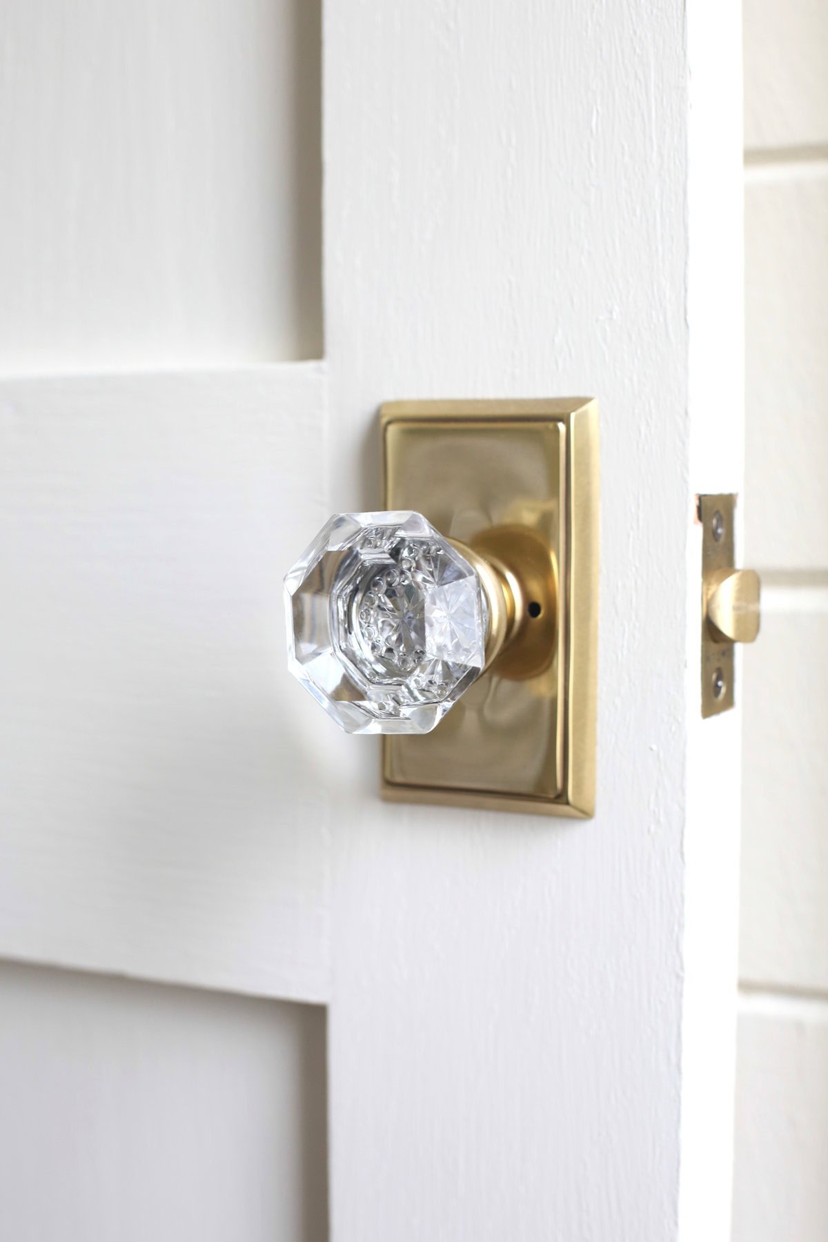 A clear glass doorknob with a brass base, mounted on a white door partially open against a white wall.