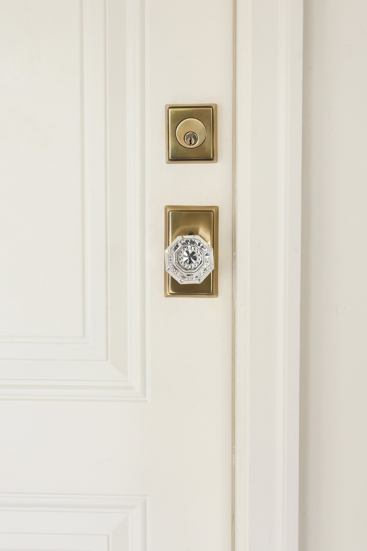 A white door featuring a brass lock and brass door knobs on square brass plates.