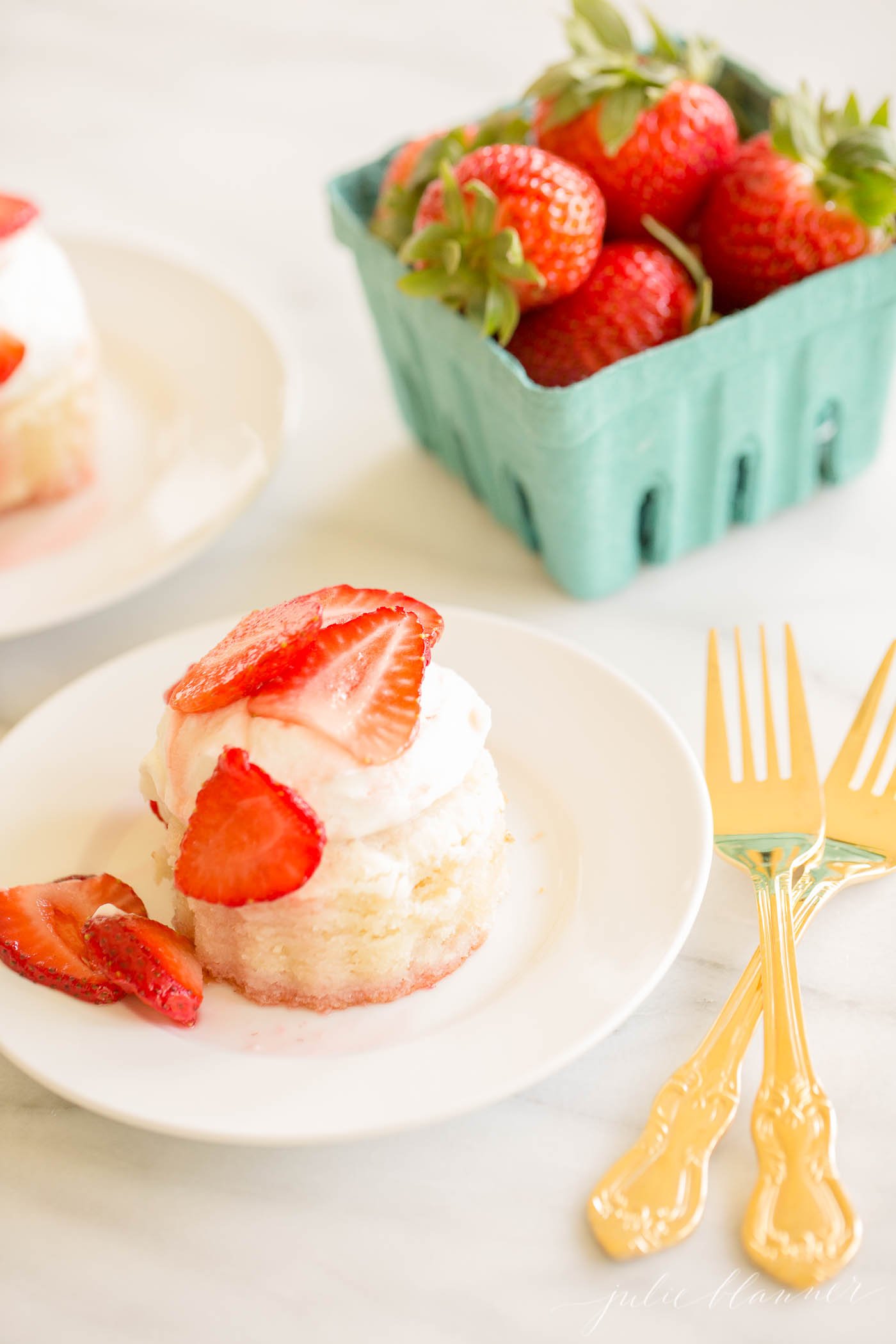 A white plate with strawberry shortcake and a small container of fresh strawberries behind.